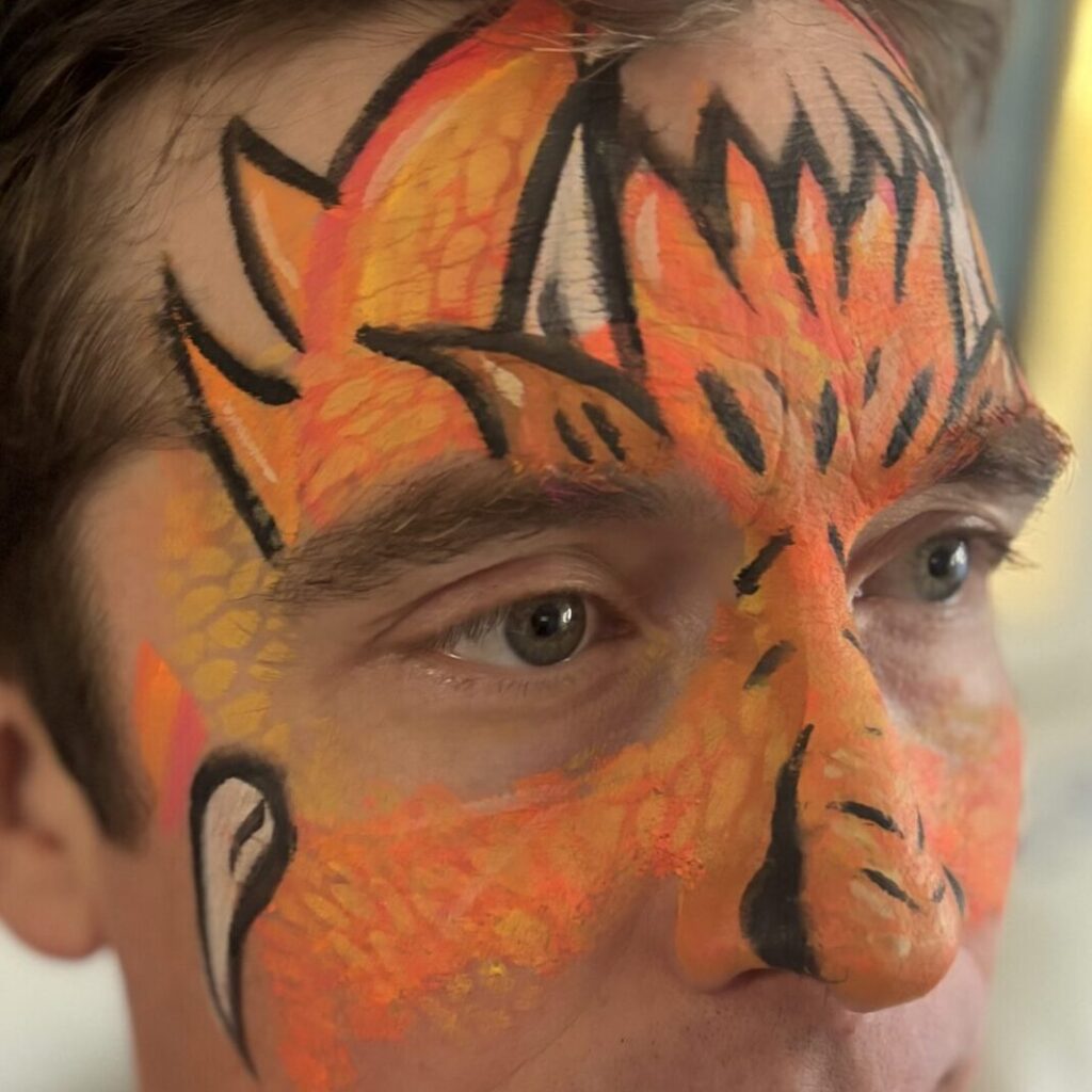 Adult male with face painted as an orange dragon with horns.