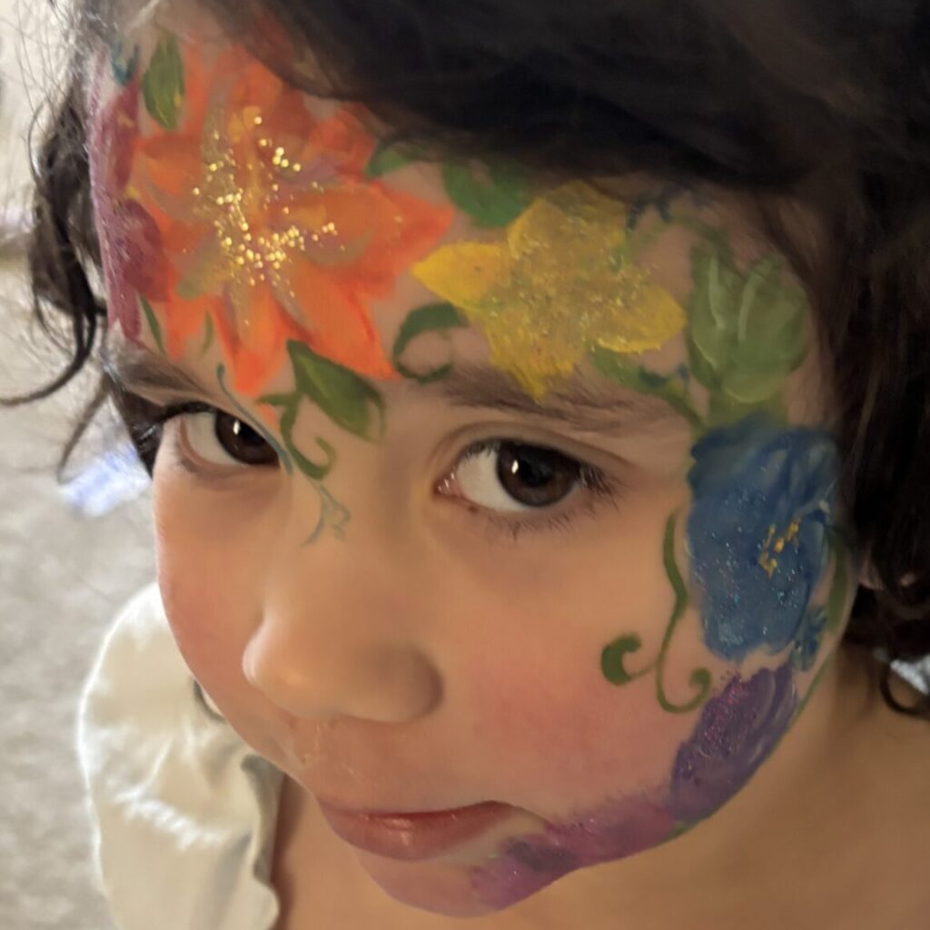Colorful floral face painting in orange, yellow, blue, and purple on a young girl