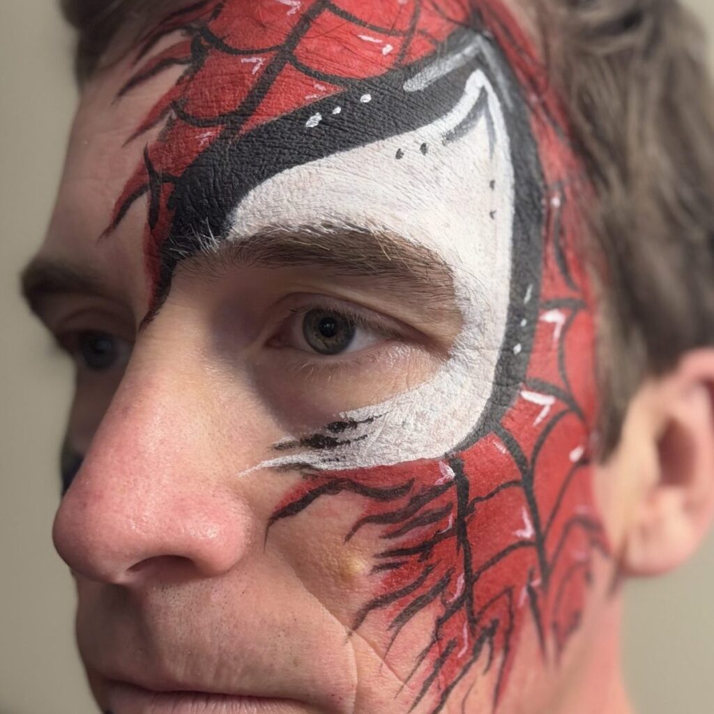 Adult male with face painted with a torn Spiderman mask.